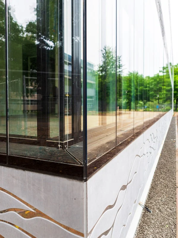 detail van gevelbekleding met gegraveerde stromingslijnen in beton weerspiegelend in het glas
